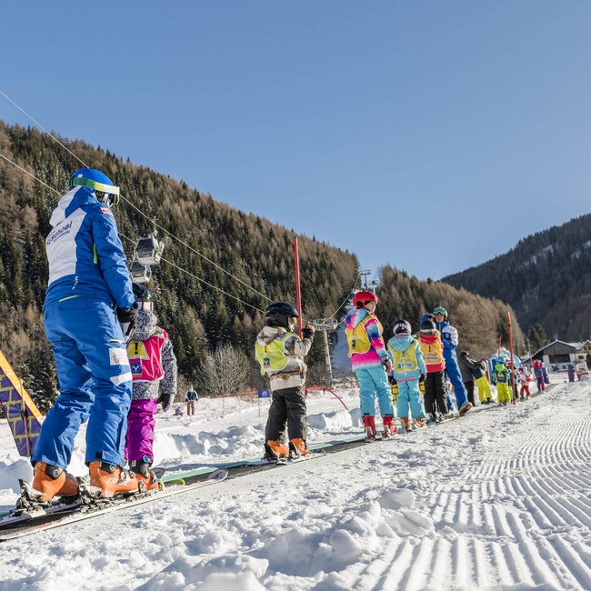 Skifahren in Südtirol: Gitschberg Jochtal Skikinder und Lehrer auf Förderbandlift im sonnigen Skigebiet