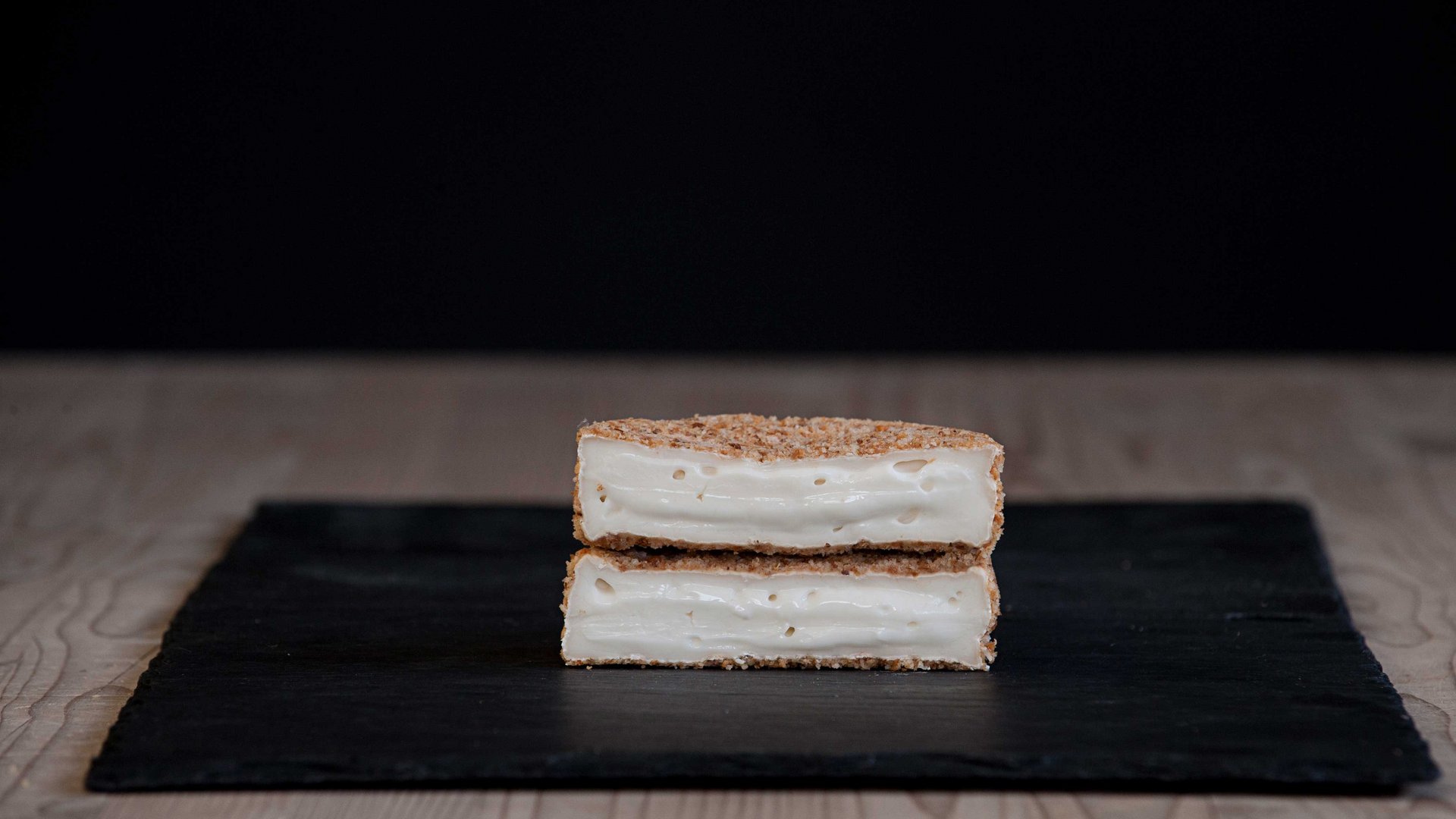 De Feinkäserei Capriz De foto toont twee opgestapelde, gehalveerde stukjes knapperig brood of paneermeel, gevuld met gesmolten kaas. De kaas is zacht, romig en rekt licht uit. Het geheel geeft de indruk van een knapperig gebakken kaas snack.