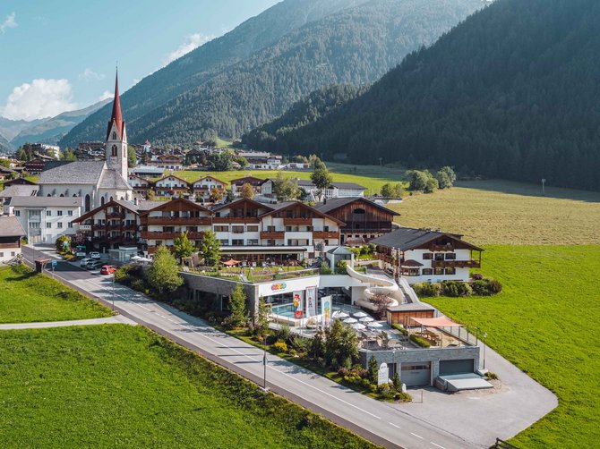 Willkommen in der Ferienregion Gitschberg Jochtal! Blick auf ein Dorf mit Kirche und alpinem Hintergrund bei Sonnenschein