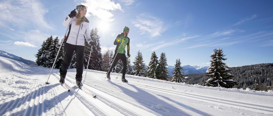 Find your accommodation in South Tyrol Two people cross-country skiing on snowy trail in bright sunlight