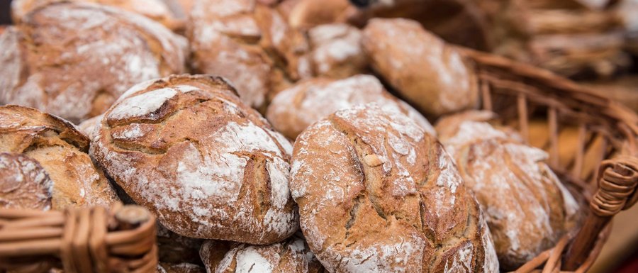 Find your accommodation in South Tyrol The picture shows a basket full of freshly baked breads with a crispy crust and a slightly floured surface. A hand is reaching for one of the breads, indicating a sale or selection.