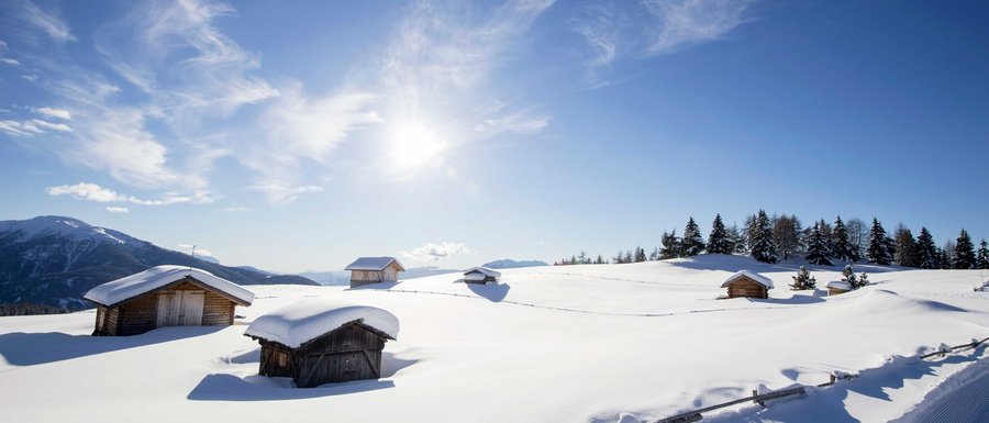 Find your accommodation in South Tyrol Snow-covered wooden huts on sunny mountain under clear blue sky