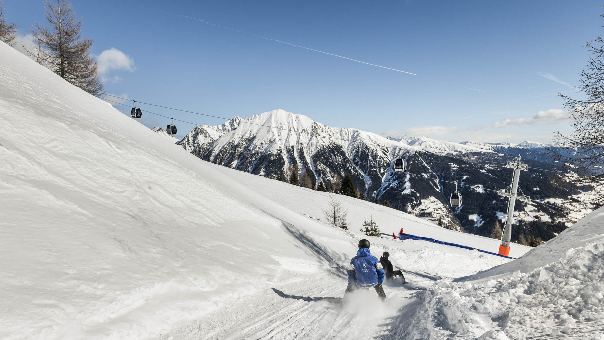 Skigebied Gitschberg Jochtal Mensen roetsjen op besneeuwde helling met kabelbanen en bergen op achtergrond