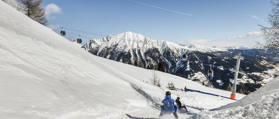 Find your accommodation in South Tyrol People sledding on snowy slope with cable cars and mountains in background