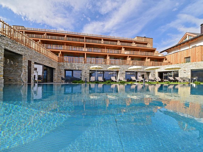 Willkommen in der Ferienregion Gitschberg Jochtal! Moderner Hotelpool mit Liegestühlen und Holzfassade bei sonnigem Wetter