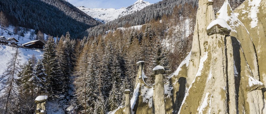 Find your accommodation in South Tyrol Snow-covered earth pyramids with forested mountains and blue sky