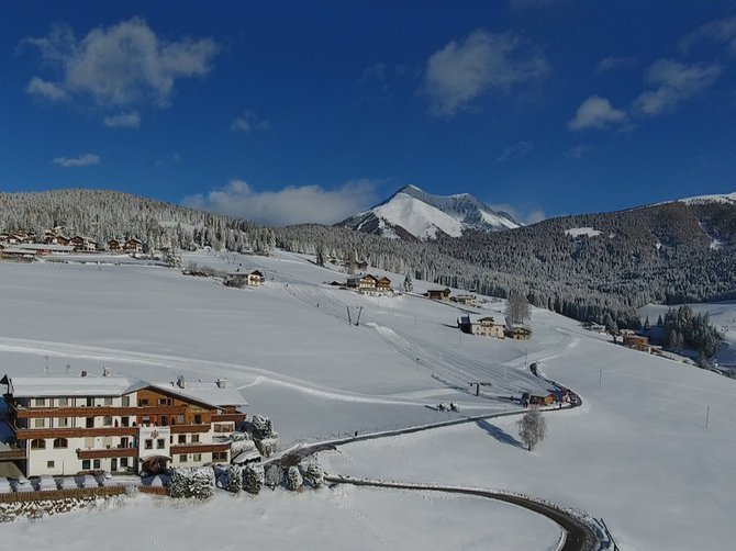 Willkommen in der Ferienregion Gitschberg Jochtal! Winterlandschaft mit verschneitem Hotel und Bergen unter blauem Himmel