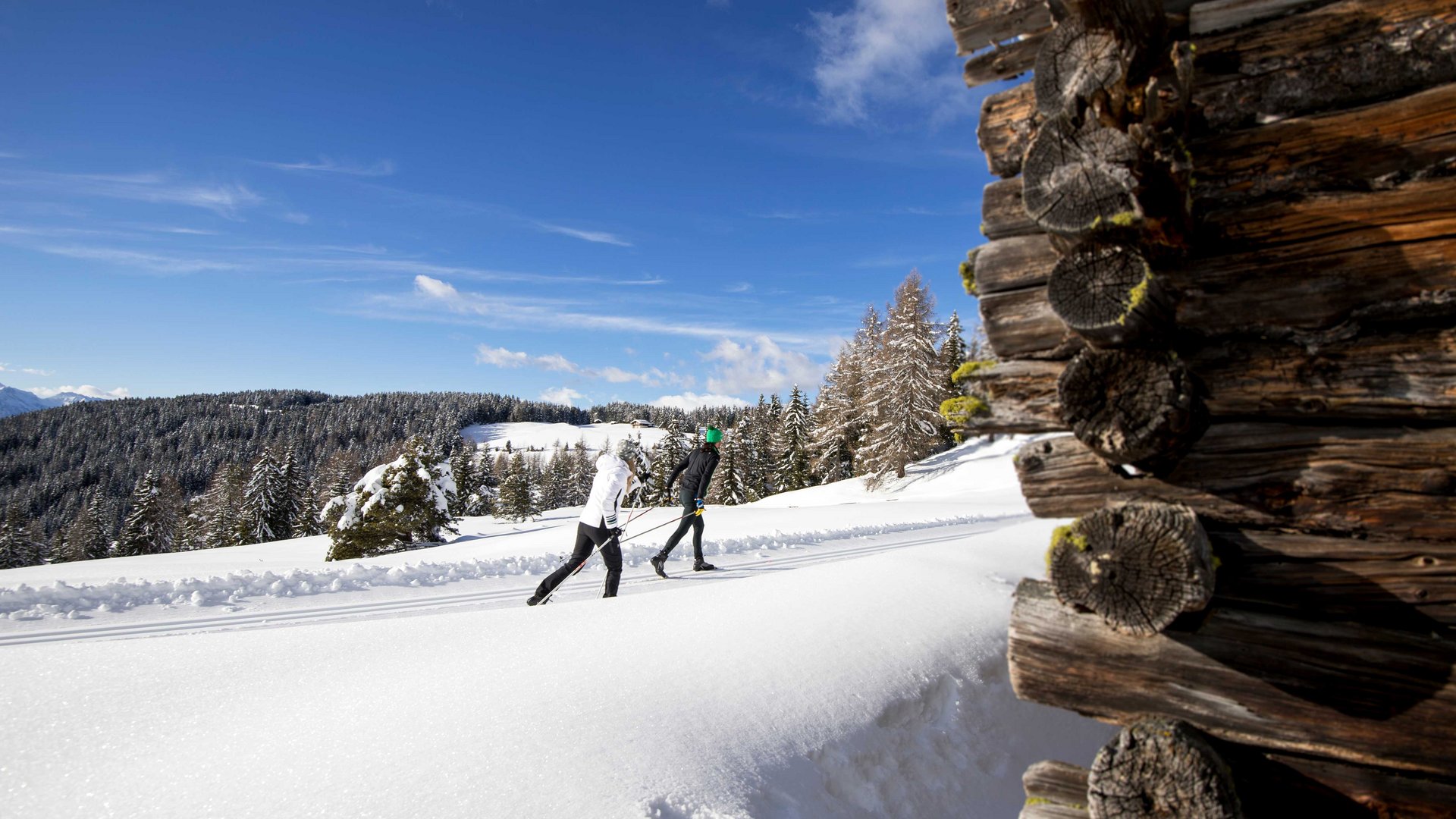 De Rodenecker-Lüsner Alm Twee langlaufers op besneeuwd pad naast houten blokhut