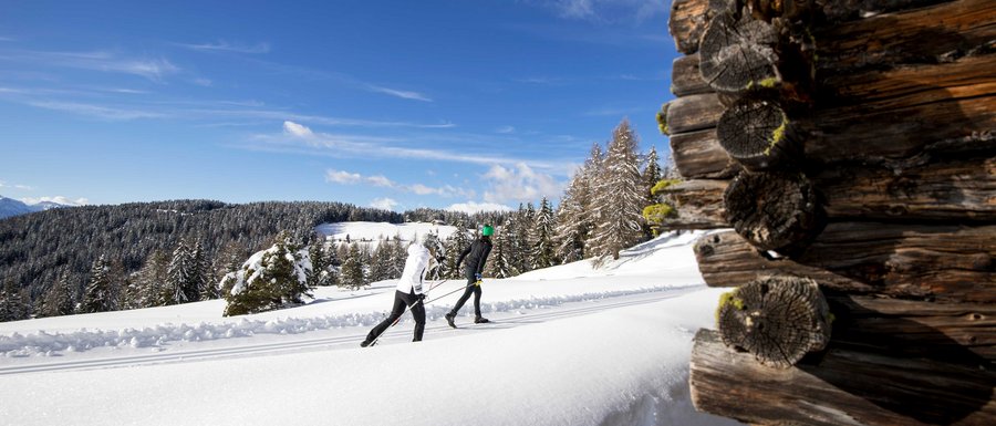 Find your accommodation in South Tyrol Two cross-country skiers on snowy trail beside wooden cabin