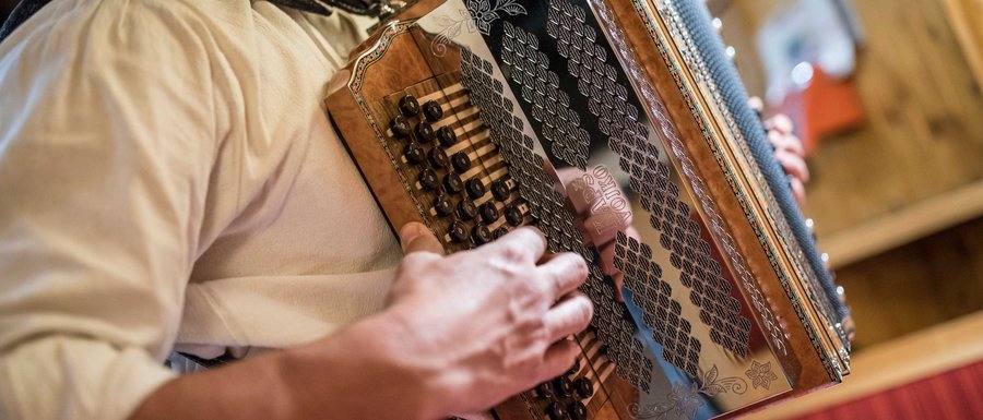 Find your accommodation in South Tyrol The picture shows a person playing a traditional accordion. The focus is on the hands operating the buttons and keys of the instrument, while the accordion features detailed decorations.