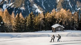 De Rodenecker-Lüsner Alm Twee mensen wandelen in de sneeuw bij een hut en dennenbomen in de bergen