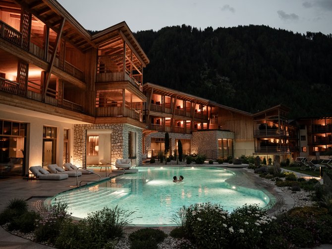Willkommen in der Ferienregion Gitschberg Jochtal! Beleuchtetes Hotel mit Außenpool und zwei Personen im Wasser bei Nacht