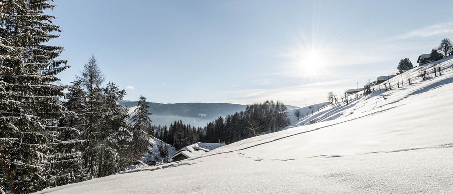 Find your accommodation in South Tyrol Snowy winter landscape with houses and trees under bright sun