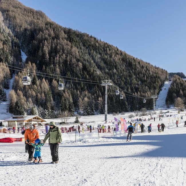 Willkommen in der Ferienregion Gitschberg Jochtal! Skigebiet mit Menschen, Skiliften und verschneiten Bergen bei klarem Himmel
