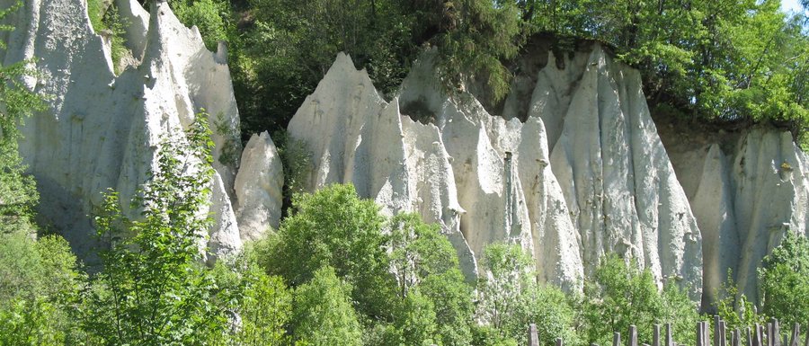Find your accommodation in South Tyrol Rock formations with wooden stake fence and green trees in sunlight