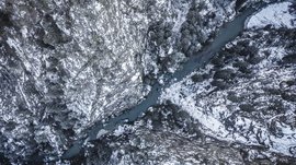 Rodeneck – for a wonderful walking holiday in Italy The image shows an aerial view of a deep gorge through which a river winds. The steep, snow-covered rock walls and the dark, barren trees along the gorge enhance the impression of a rugged, wintry wilderness.