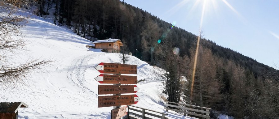 Find your accommodation in South Tyrol Hiking signpost in snowy Alpbach valley with mountain and bright sun